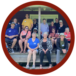 A group of brain injury survivors, their family members and biaww staff sitting on steps leading to a cottage.