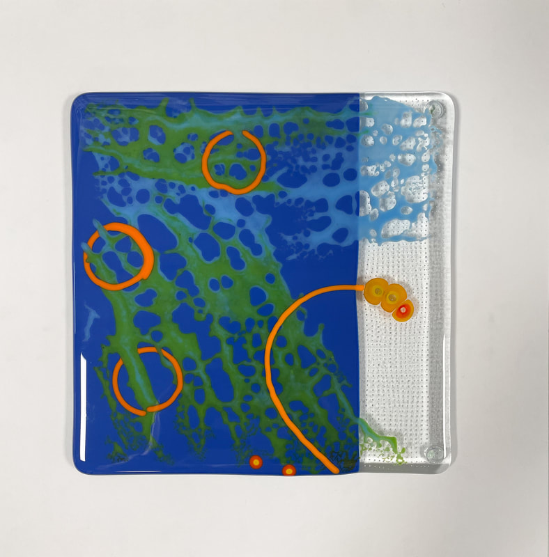 A glass tile featuring an abstract orange, green and blue swirls.