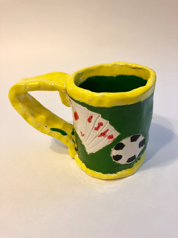 A green mug with playings cards and a poker chip on it.