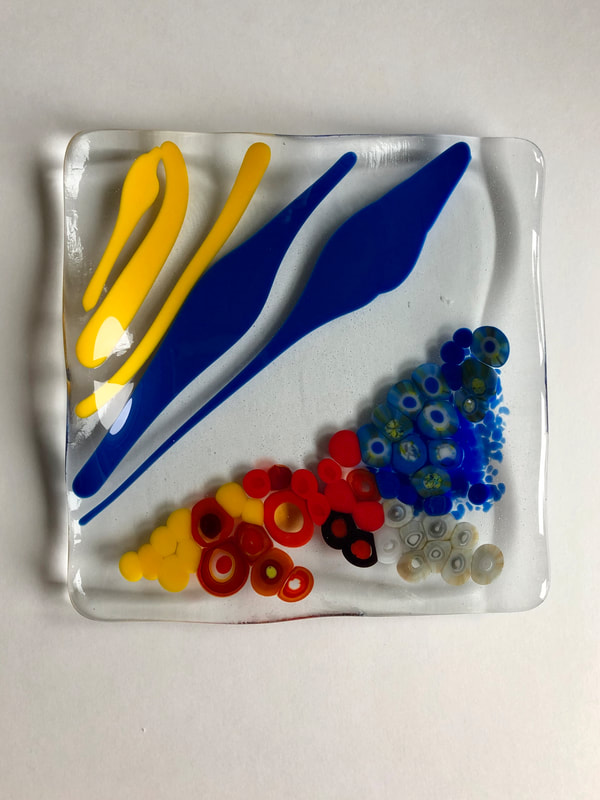 A glass tile featuring yellow and blue stripes and circles.