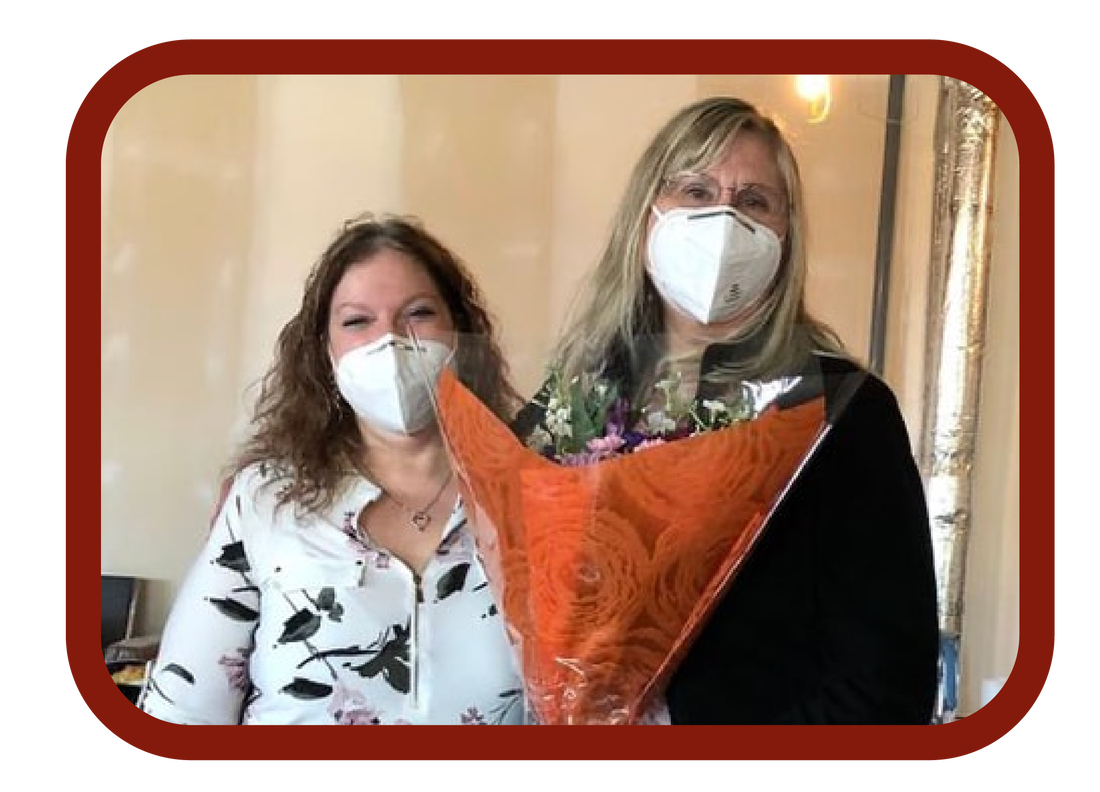 Ellen Ibele and Donna Henri smiling while wearing masks and holding a bouquet of flowers.