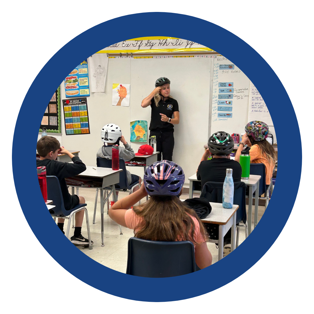 A BIAWW member giving a school presentation about helmet safety to a group of children wearing bike helmets.